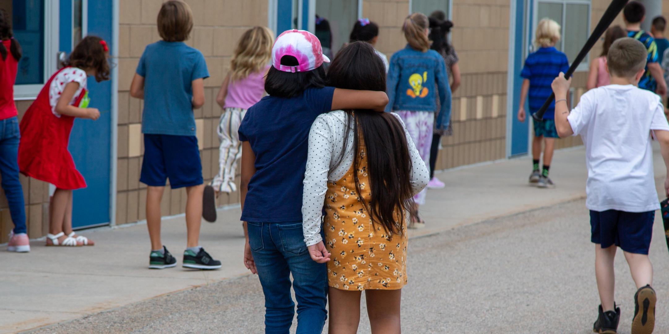 Two students walk to school with their arms around each other. 