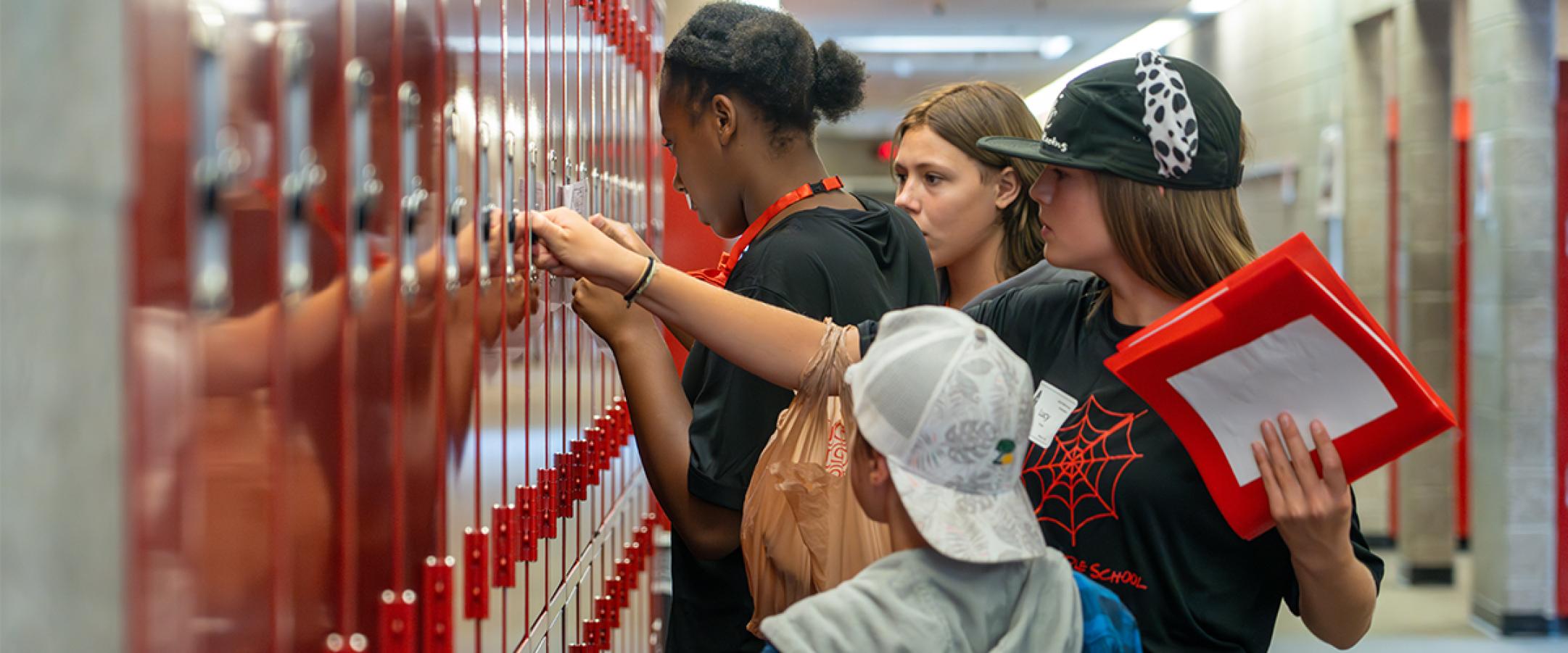 A middle school student helps a younger student open his locker.